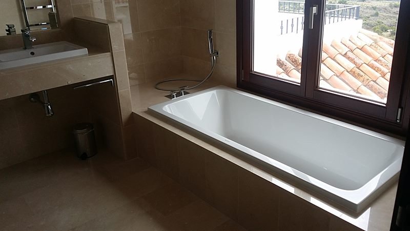 Baño principal revestido en mármol crema, con lavabo sobre encimera y bañera junto a la ventana